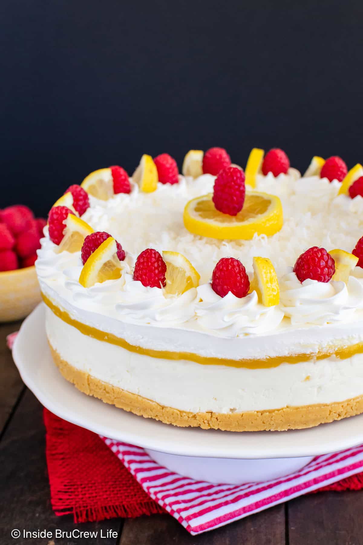 A close up of the side of a lemon coconut cheesecake topped with Cool Whip and raspberries.