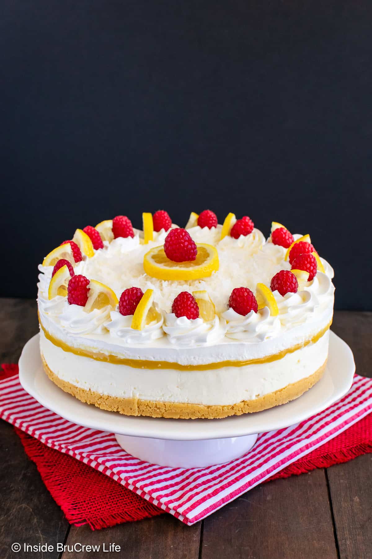 A full sized lemon coconut cheesecake on a white cake plate.
