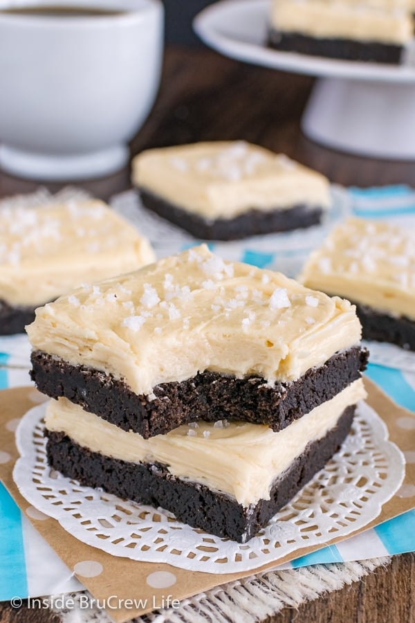 Two salted caramel chocolate sugar cookie bars stacked on a white doily with a bite taken out of the top bar