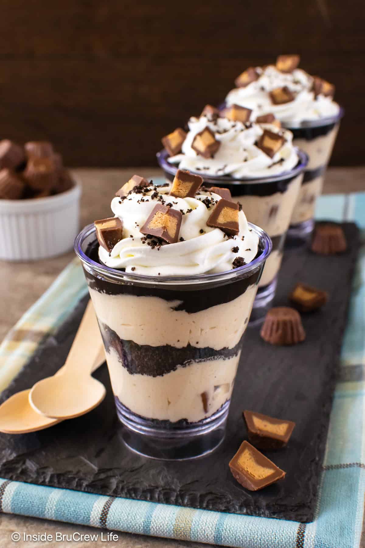 Peanut butter chocolate parfaits on a slate board with peanut butter cups on top.