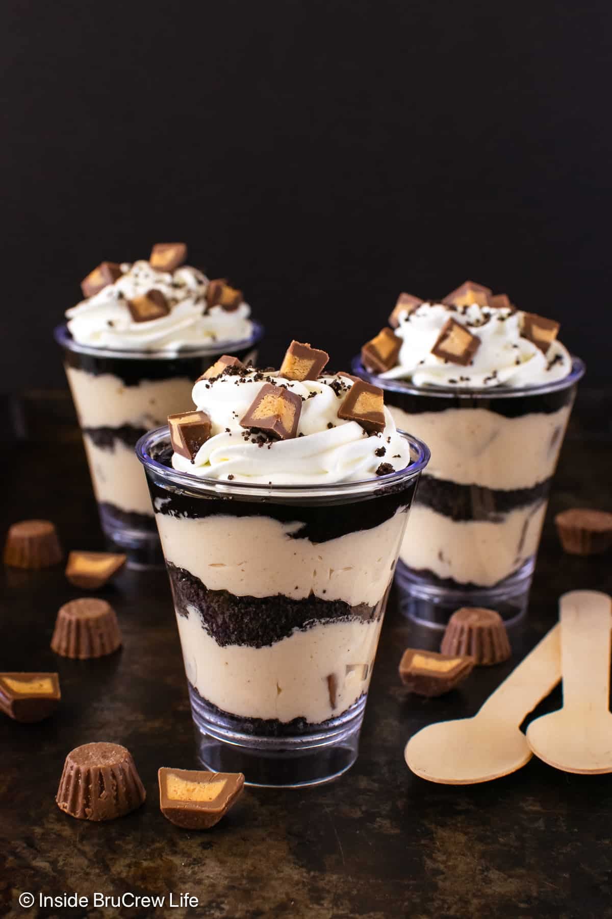 Three peanut butter chocolate parfaits topped with whipped cream and peanut butter cups.