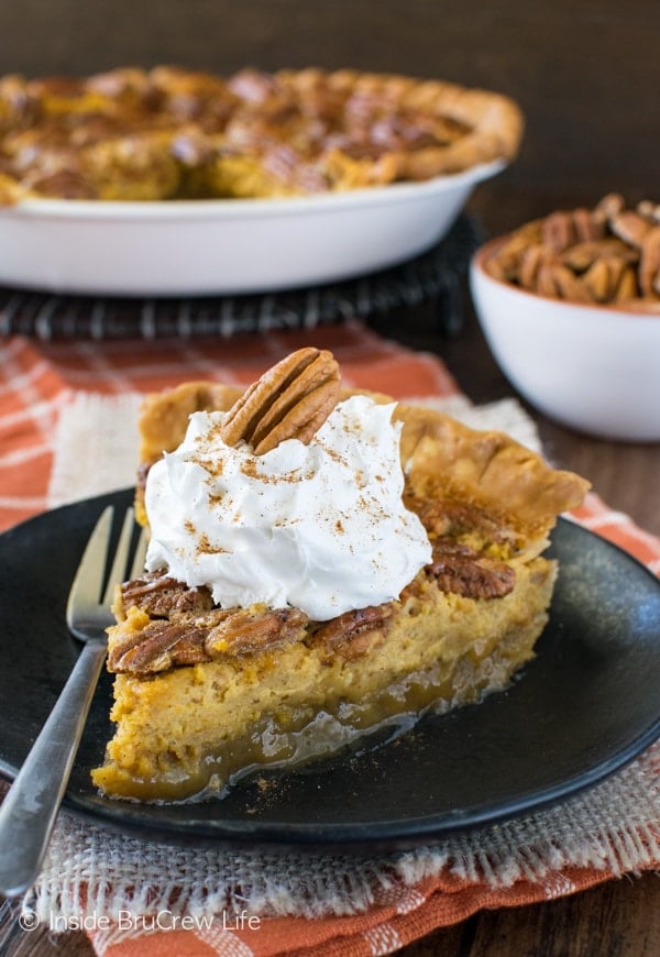 A black plate with a slice of pumpkin cheesecake pecan pie topped with whipped cream and pecans on it.