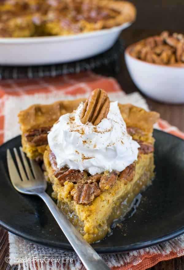 A black plate with a gooey slice of pecan pie cheesecake pie topped with whipped cream.