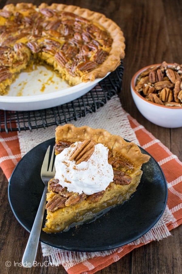 A slice of Pecan Pumpkin Cheesecake Pie on a black plate with the rest of the pie behind it