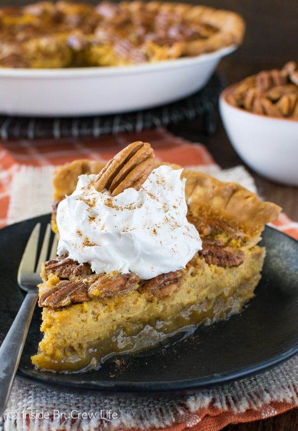 A slice of pecan pie pumpkin cheesecake on a black plate topped with pecans and Cool Whip.