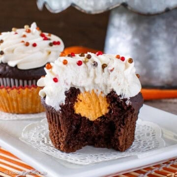 A bite out of a vanilla frosted chocolate cupcake showing the orange cream filling center.