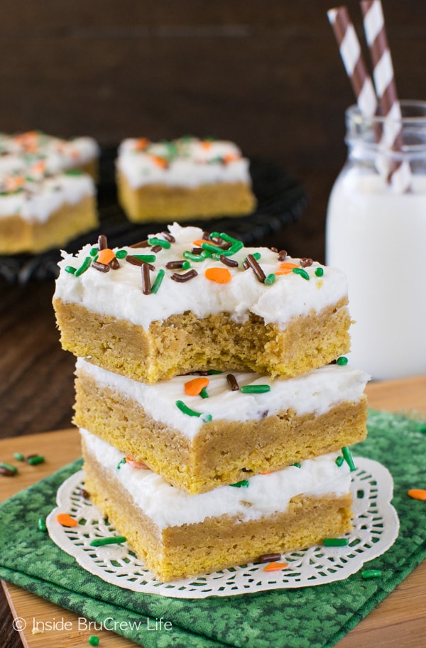 Three frosted pumpkin spice sugar cookie bars stacked on a white doily
