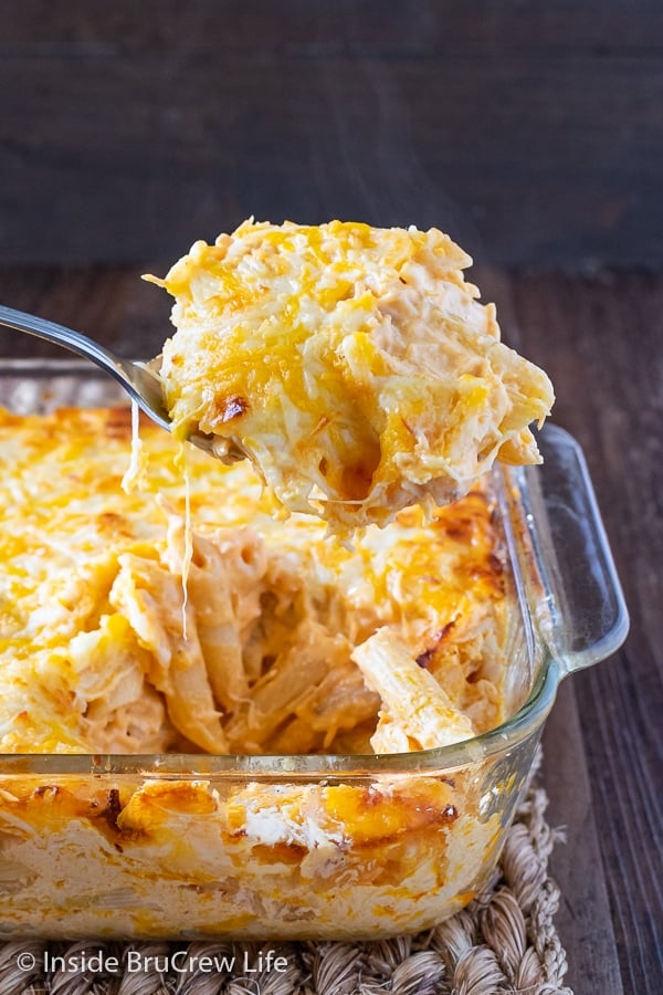 A glass baking dish filled with Buffalo Chicken Pasta Bake and a spoon lifting some cheesy pasta out.