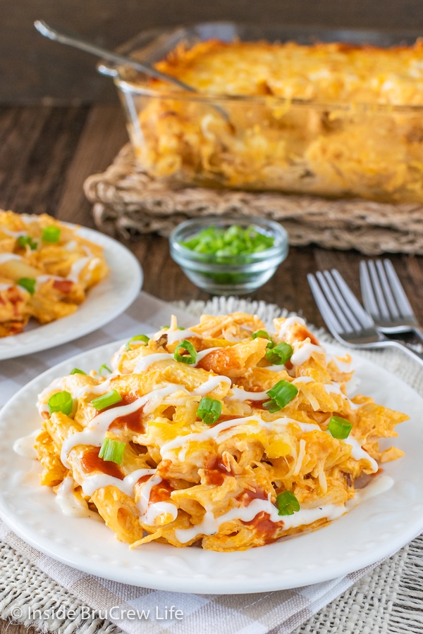 Close up picture of buffalo chicken pasta bake on a white plate and a casserole dish of pasta behind it.