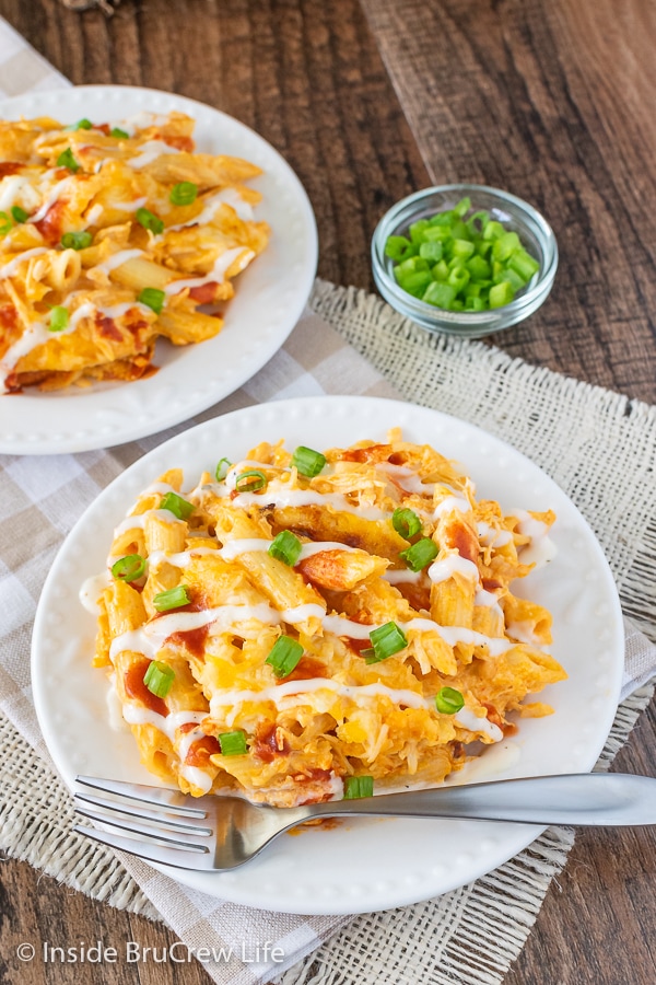 An overhead picture of a white plate with buffalo chicken pasta drizzled with ranch and hot sauce and green onions.