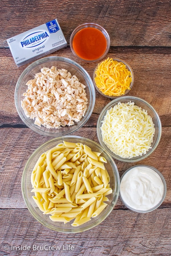 Bowls of ingredients to make buffalo chicken pasta bake on a wooden board.