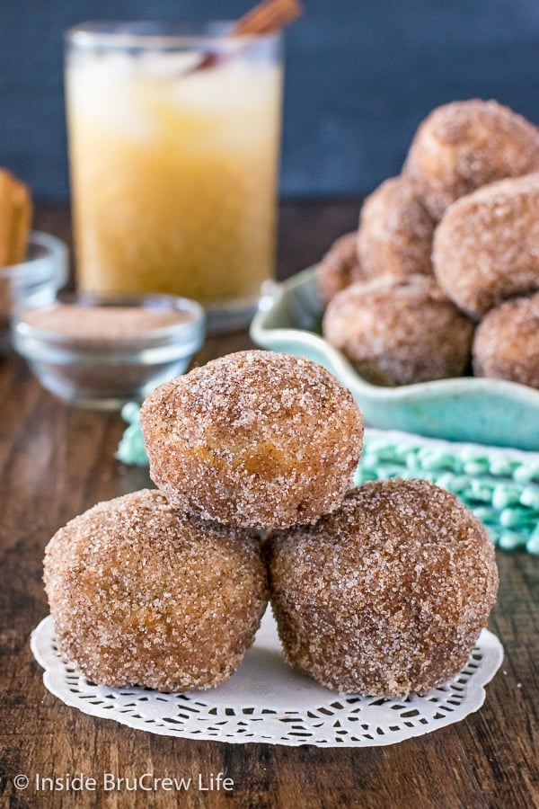 Three cinnamon sugar apple donut holes stacked on top of each other on a white paper.