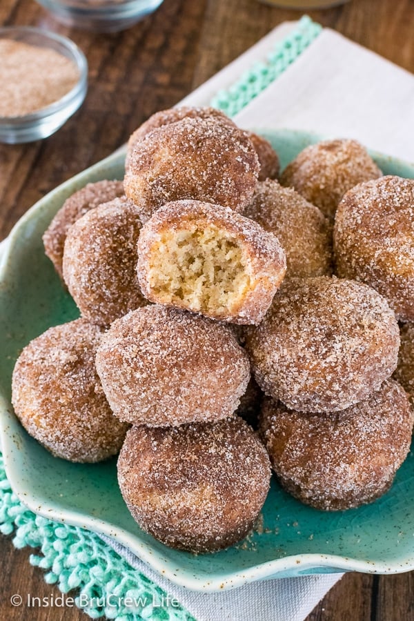 A green plate filled with cinnamon sugar apple donut holes with a bite taken out of the top donut.