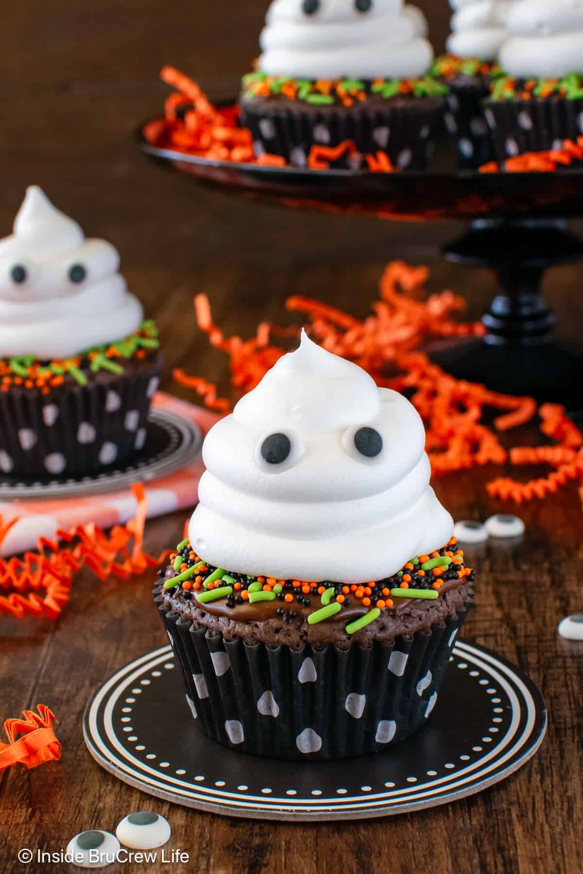 Two brownie ghost cupcakes on a brown board.