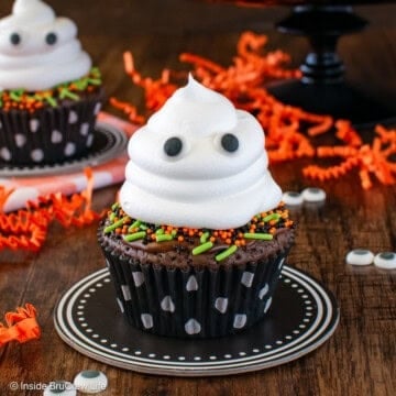 Two brownie ghost cupcakes on a brown board.