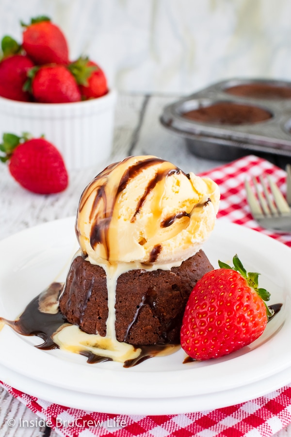 A white plate with a mini chocolate cake topped with ice cream and syrup on it.