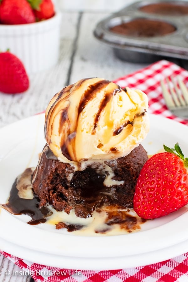 A white plate with an open chocolate lava cake topped with vanilla ice cream on it.