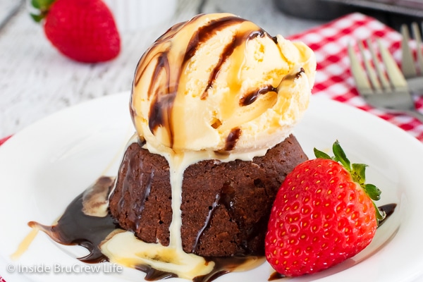 A chocolate melting cake on a white plate topped with ice cream and syrup.