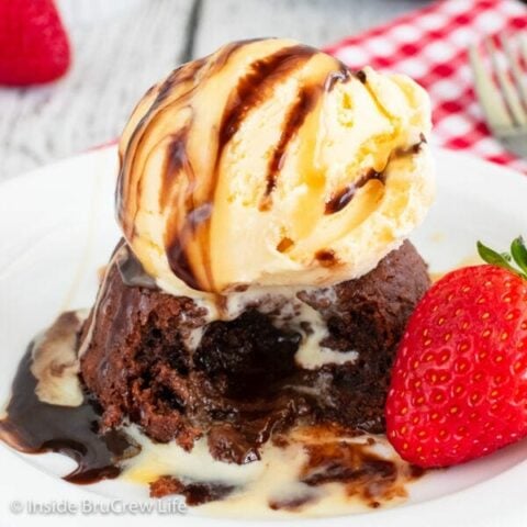 A gooey chocolate cake topped with vanilla ice cream and chocolate syrup on a white plate.