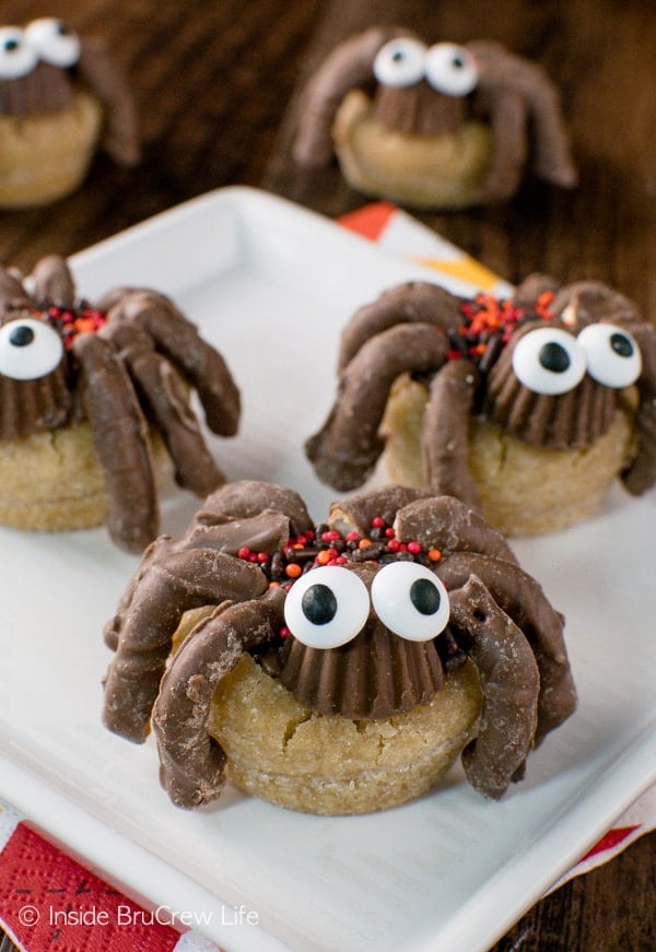 Three peanut butter cup spider cookies with googly candy eyes on a white plate