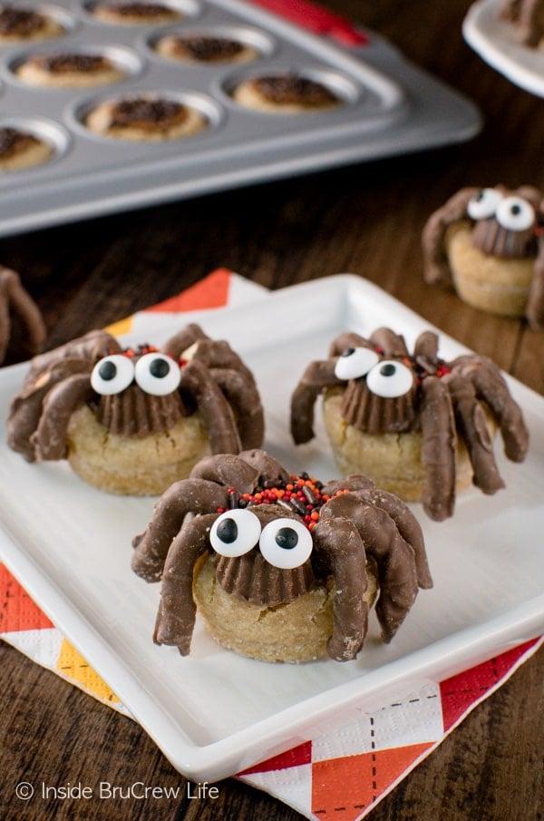 A white plate with three peanut butter cup spider cookies on it and a pan of cookies behind them