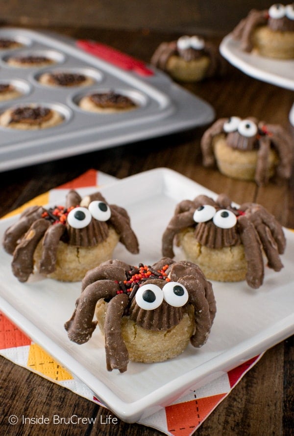 A white plate with peanut butter cup spider cookies with candy eyes on it and a pan of cookies behind it