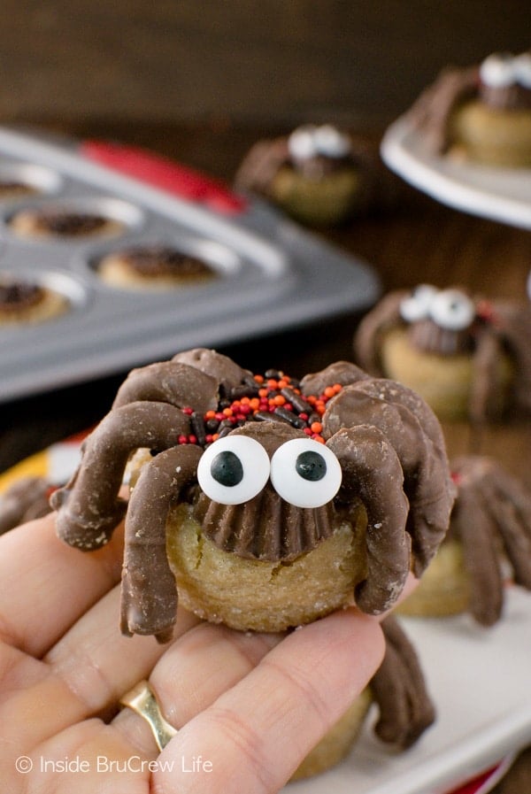 A peanut butter cup spider cookie with candy eyese held up over a plate of cookies