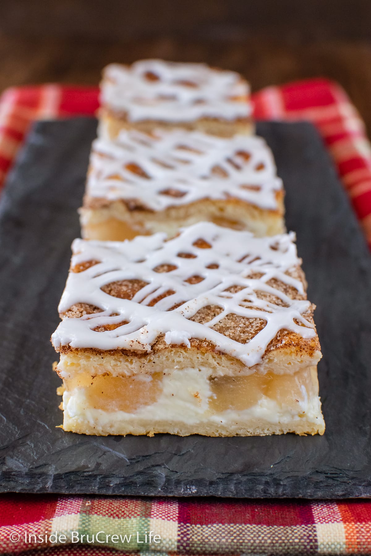 Three cream cheese apple bars on a black tray.