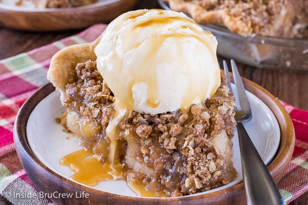 A piece of apple crisp pie with vanilla ice cream and caramel topping on a white plate
