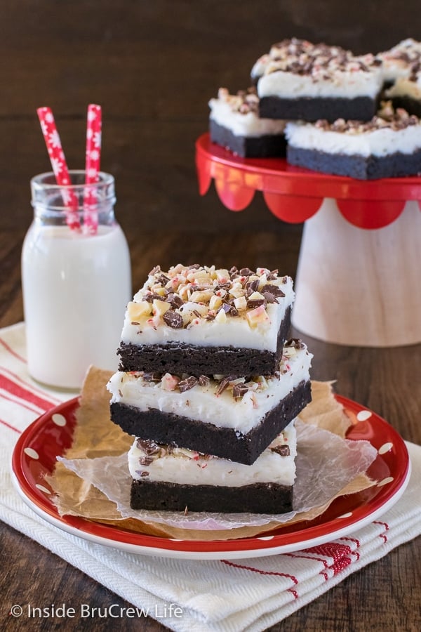 A red plate with a stack of three frosted chocolate peppermint sugar cookie bars on it and a glass of milk beside it