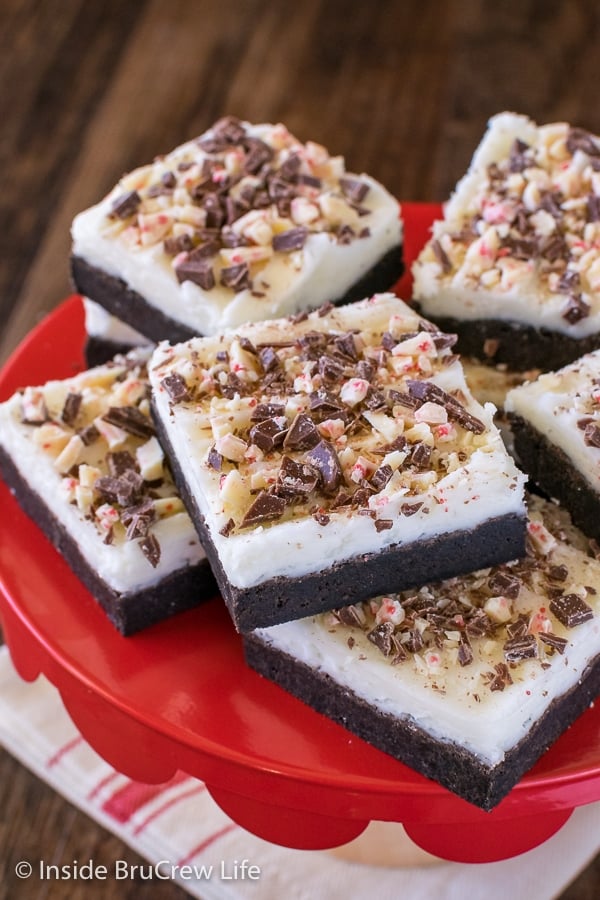 A red cake plate with squares of frosted chocolate peppermint sugar cookie bars stacked on it