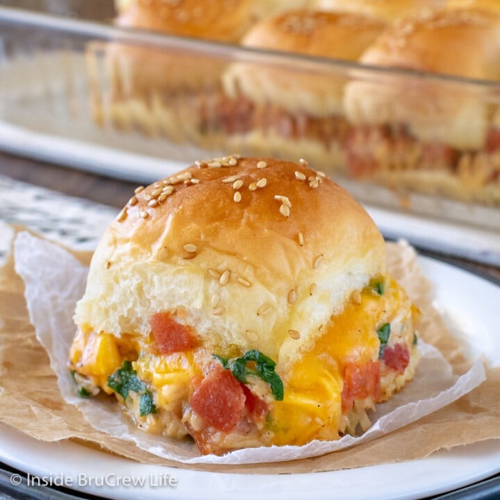 A cheesy chicken slider stuffed with chicken, veggies, and cheese on a white plate