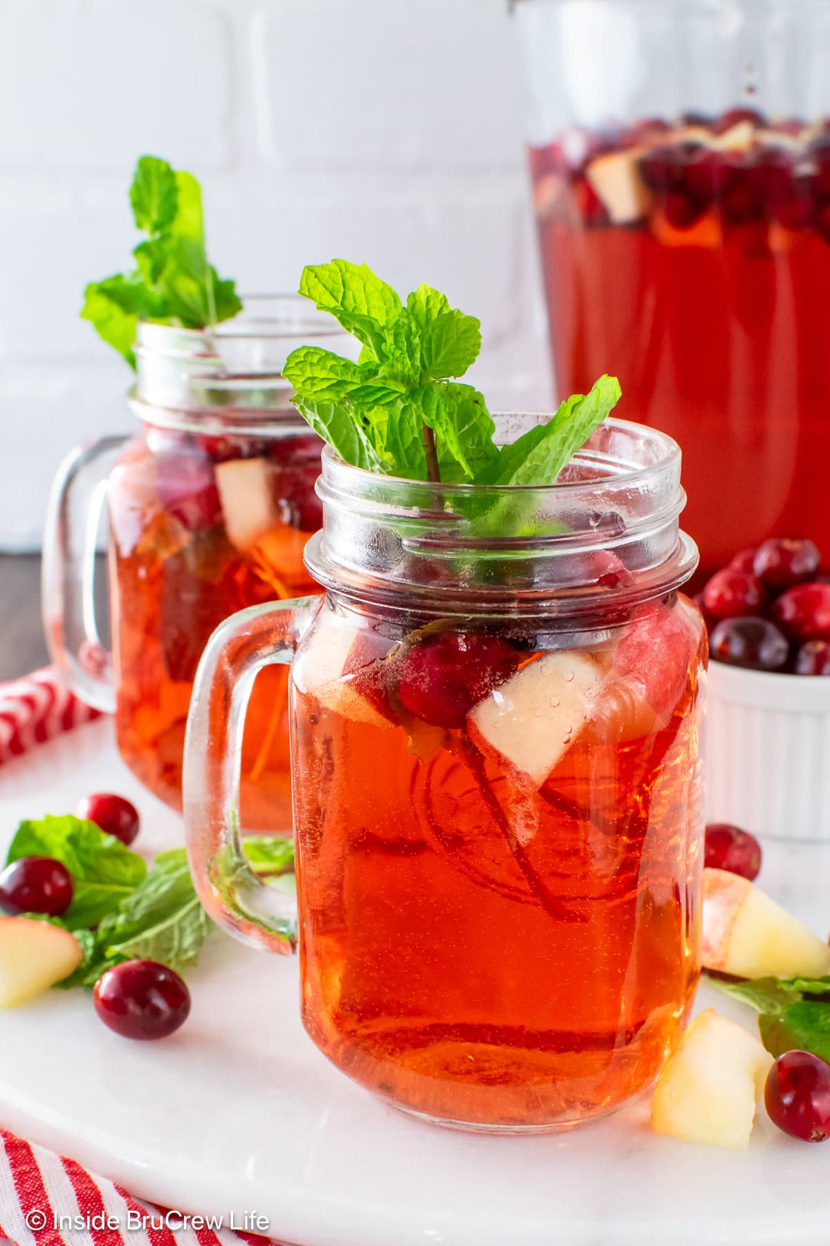 Two clear mugs filled with cranberry punch and floating fruit.