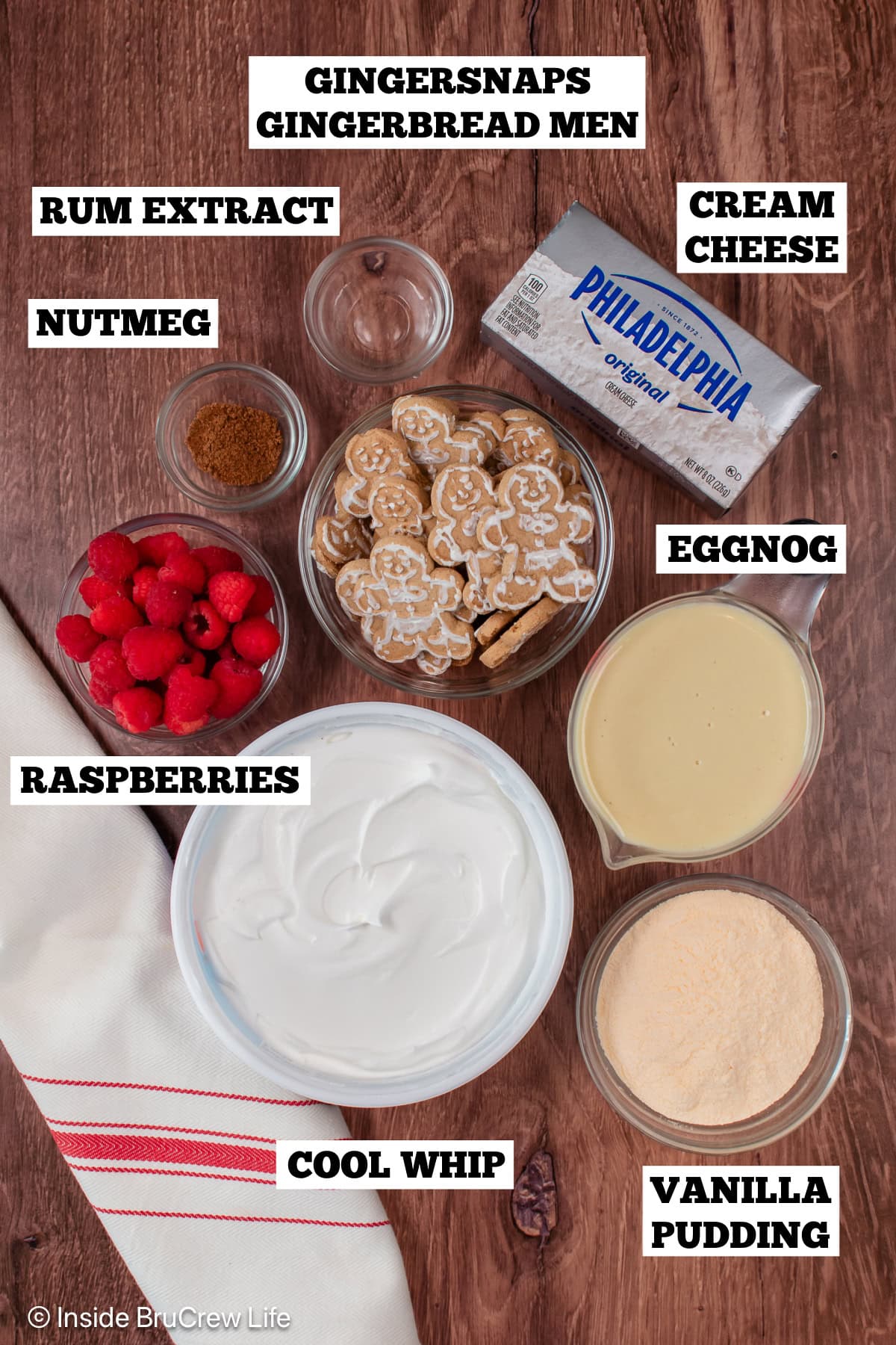 A brown board with bowls of ingredients needed to make a cookie trifle with eggnog and raspberries.