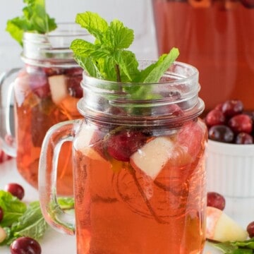 Two clear glasses filled with cranberry punch, fruit, and mint leaves
