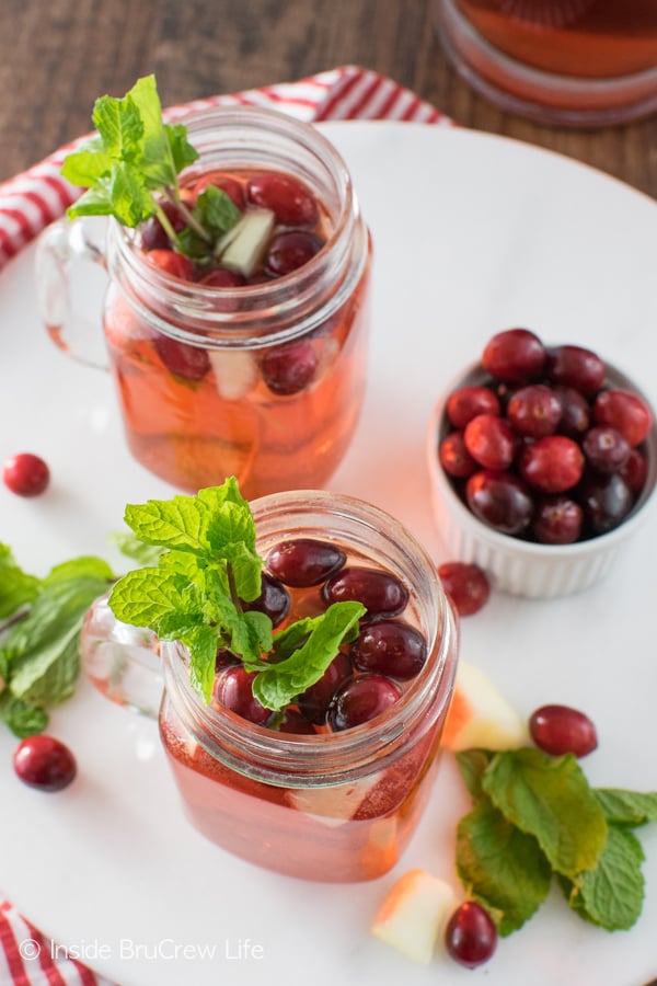 A white tray with two glasses filled with cranberry punch, fresh cranberries, and mint leaves on it