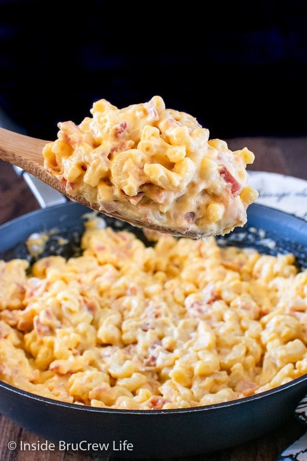 A skillet of cheesy pasta with a spoonful in the air.