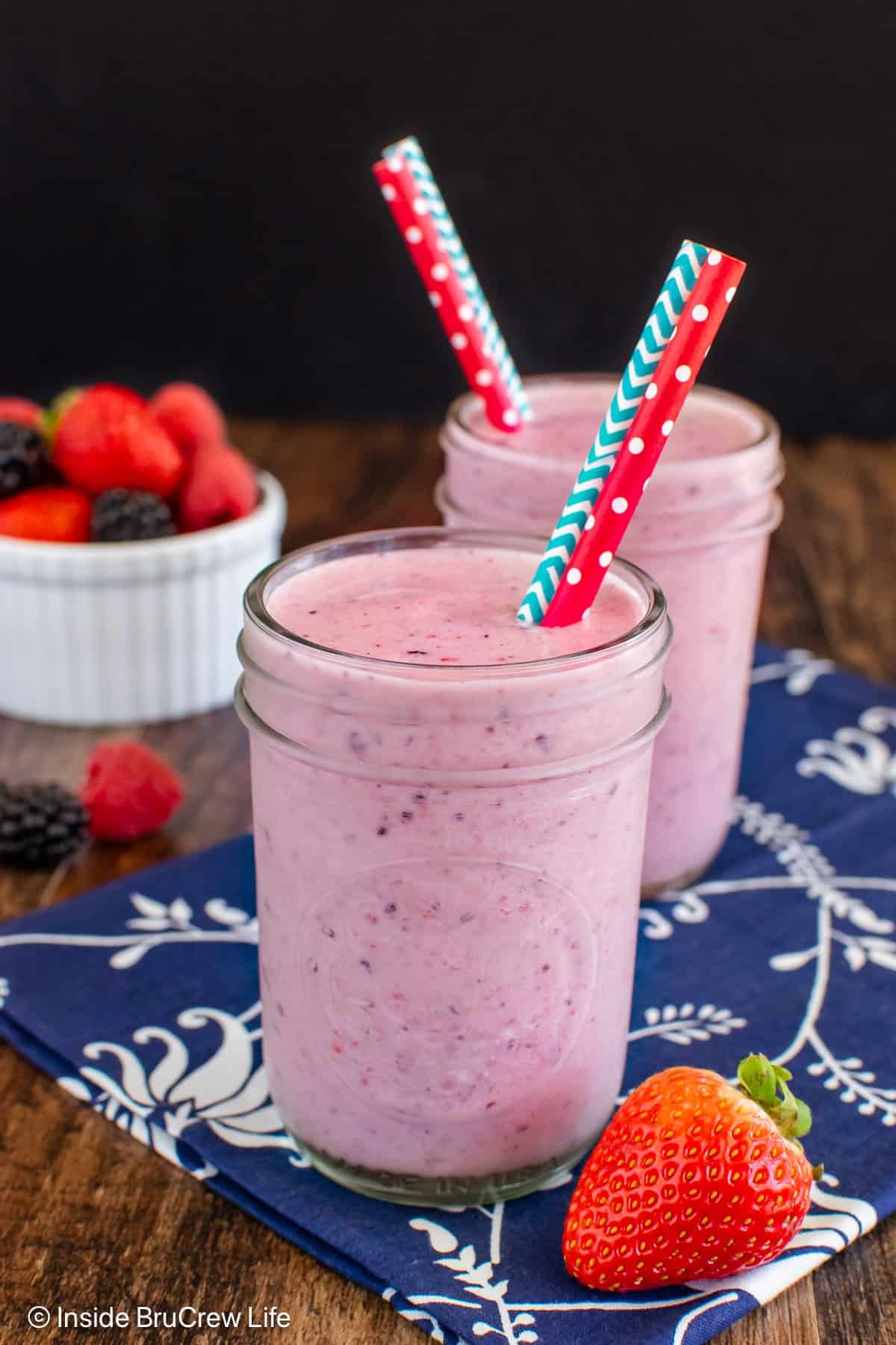 Two clear cups filled with a pink berry orange smoothie.