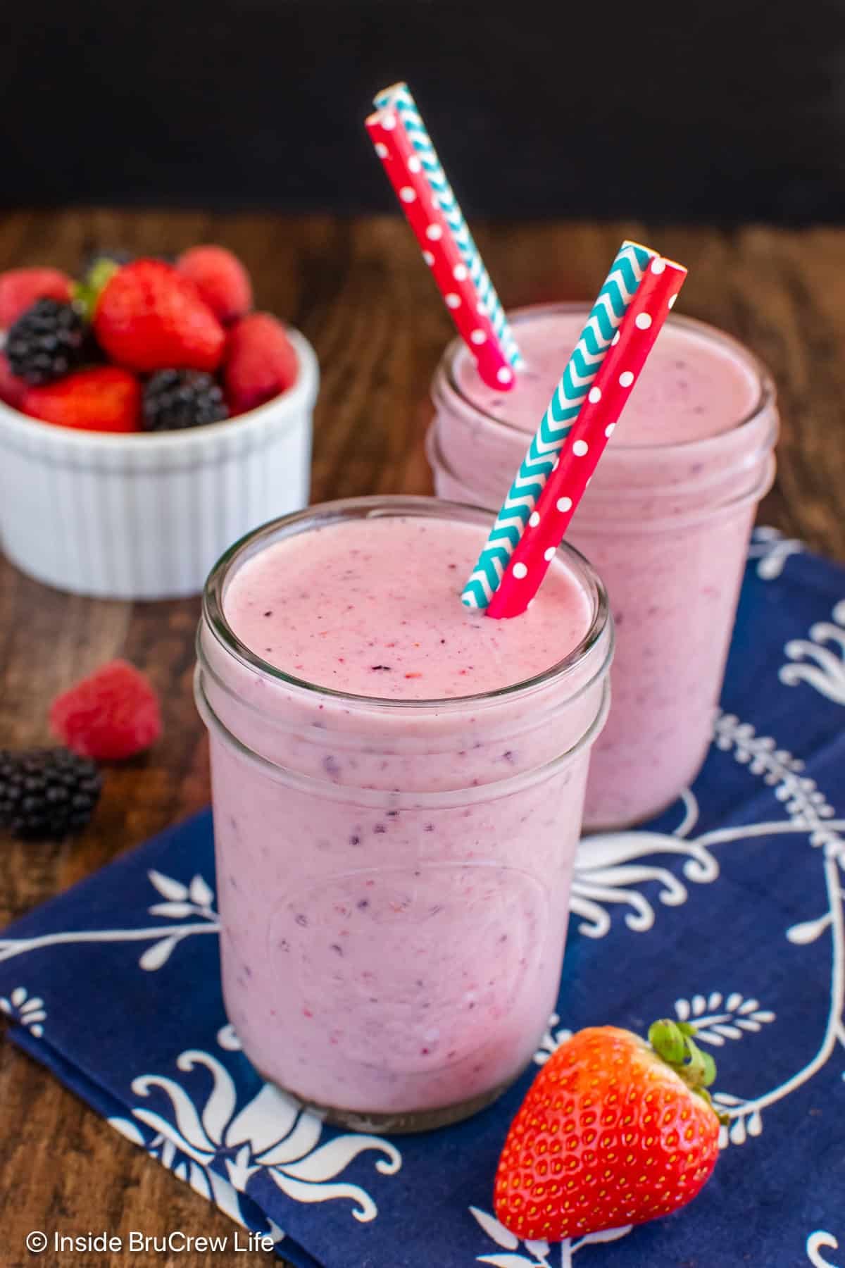A pink berry orange smoothie served in two glass cups with straws.