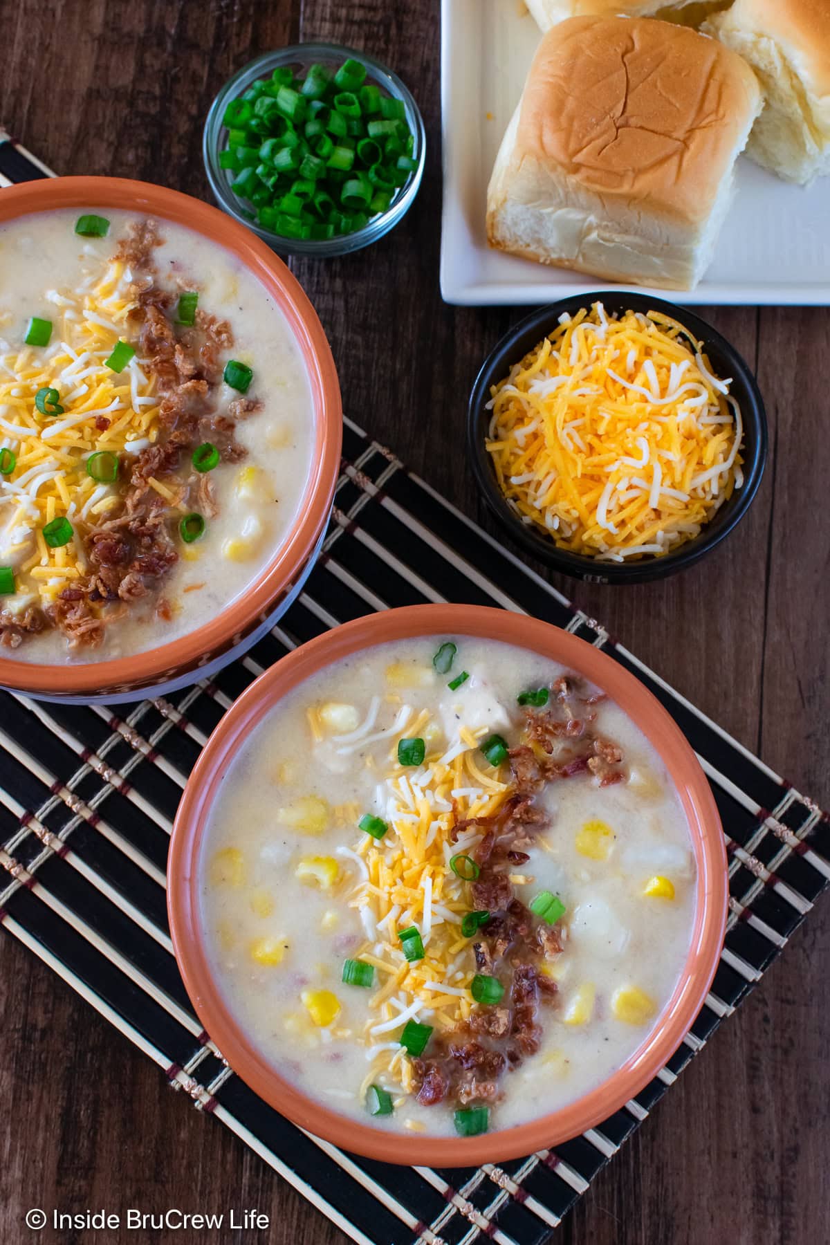 Two bowls of chicken corn chowder topped with bacon and shredded cheese.