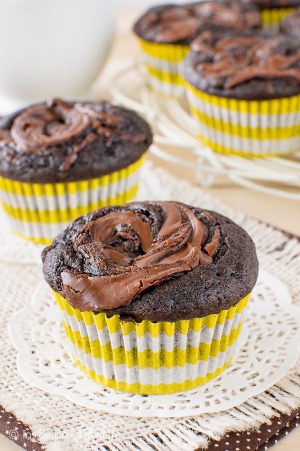 Two chocolate nutella banana muffins in white and yellow liners sitting on white doilies