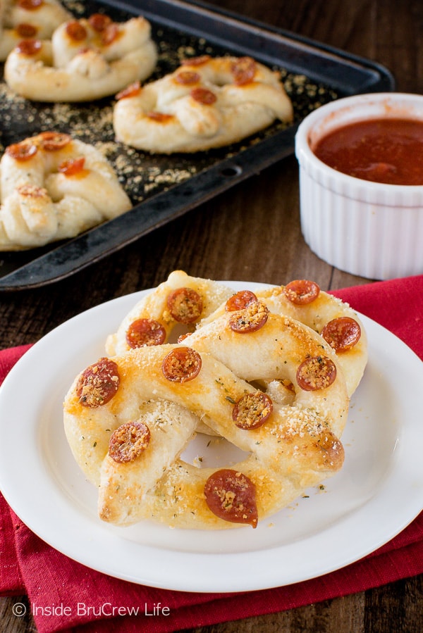 A white plate with 3 pepperoni cheese pretzels on it.