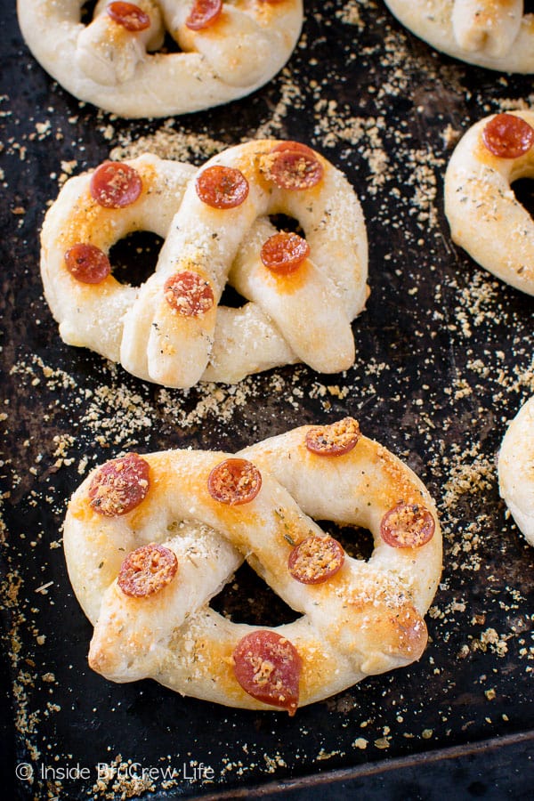 A dark pan with home made pepperoni pretzels on it covered in parmesan cheese.