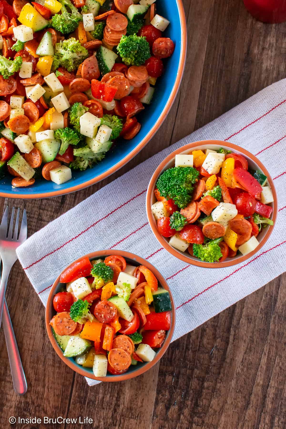 Bowls of chopped veggie salad on a brown board.