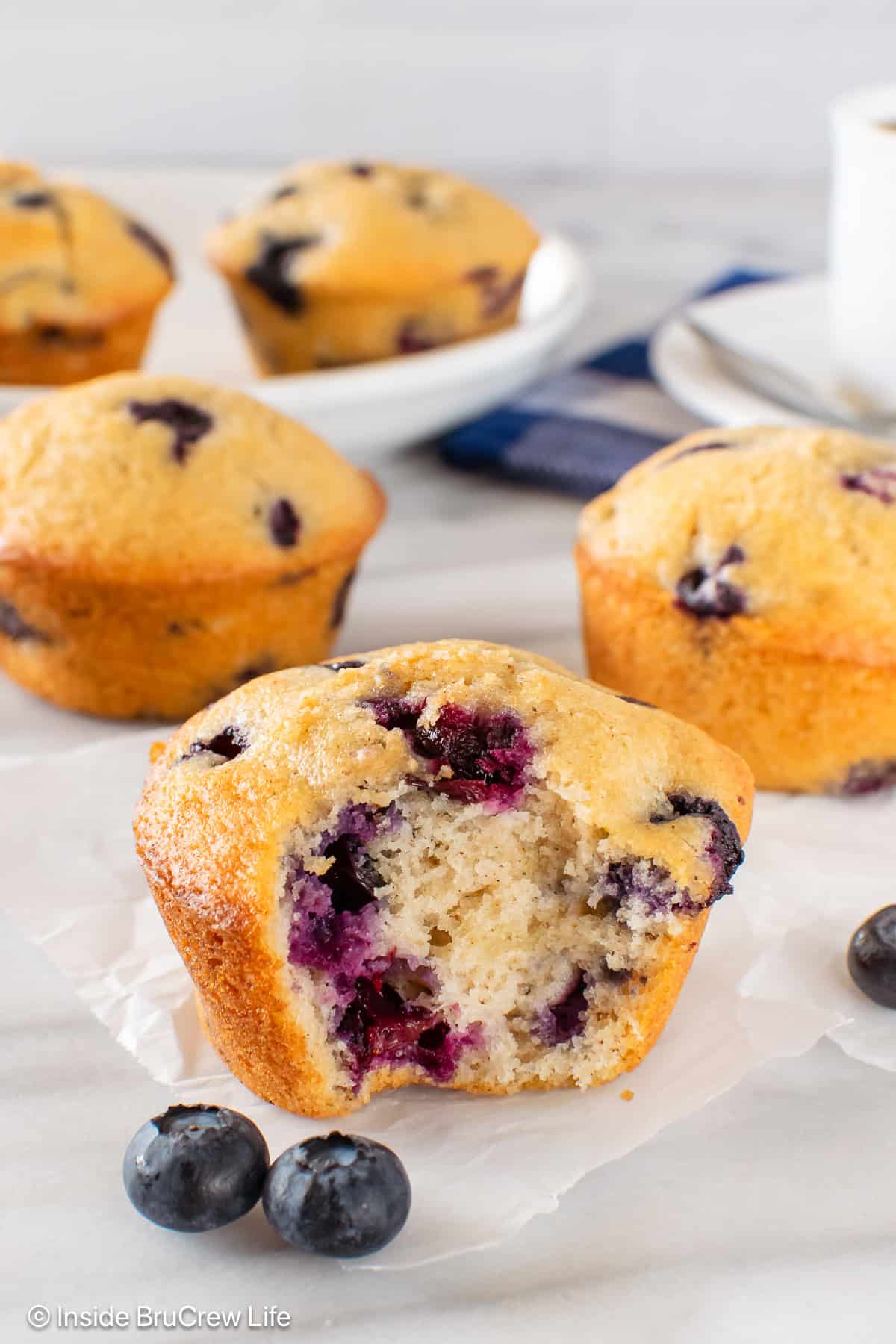 Blueberry muffins on a white board and the front one has a bite out of it.
