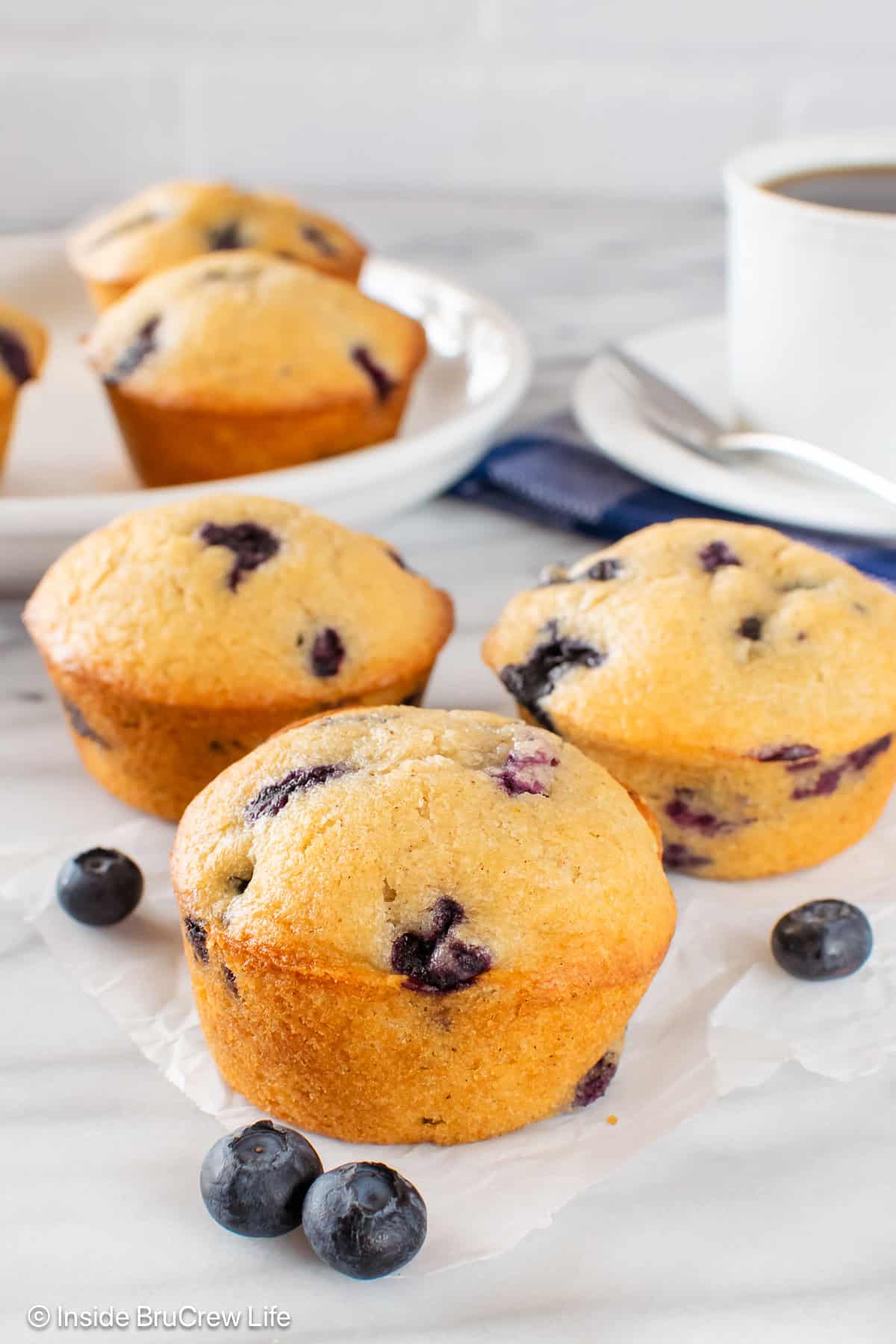Three fluffy sour cream blueberry muffins on a white board.