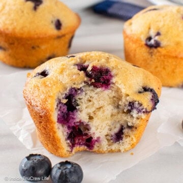 A sour cream blueberry muffin with a bite out of the front of it.