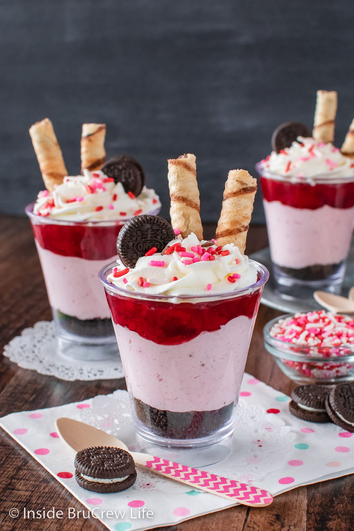 Clear cups filled with chocolate cookie crumbs, no bake strawberry cheesecake, and strawberry pie filling.