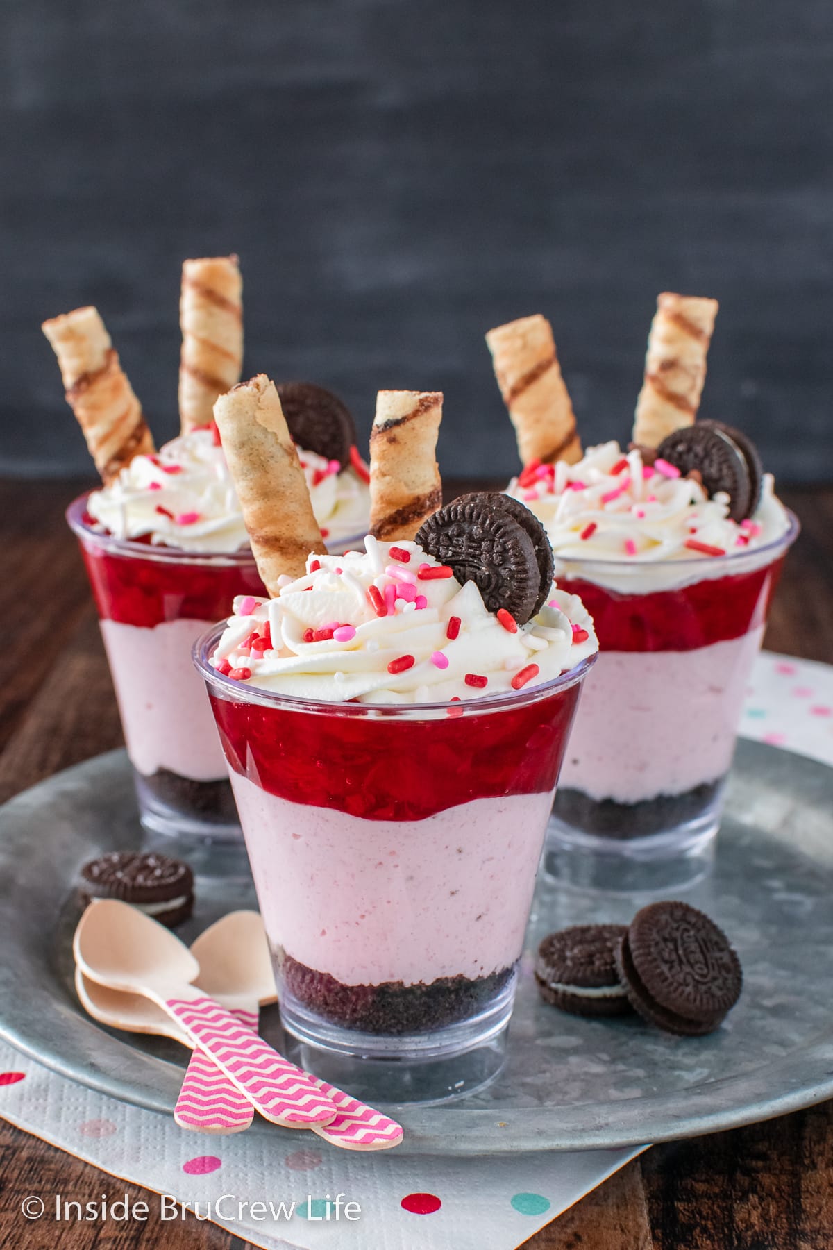 Three clear cups filled with strawberry cheesecake, cookie crumbs, and pie filling.