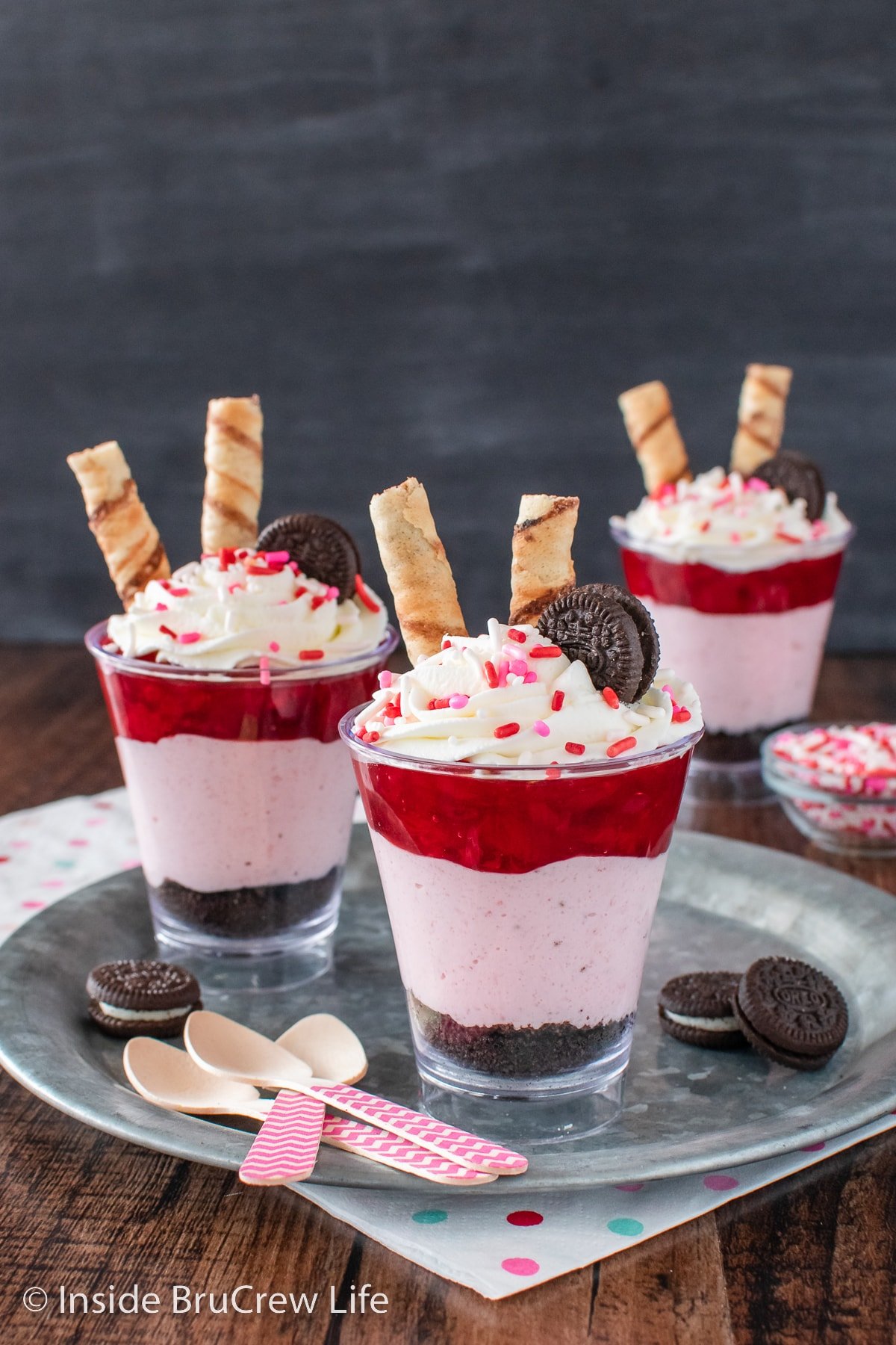 Clear cups filled with chocolate cookie crumbs, no bake strawberry cheesecake, and strawberry pie filling.